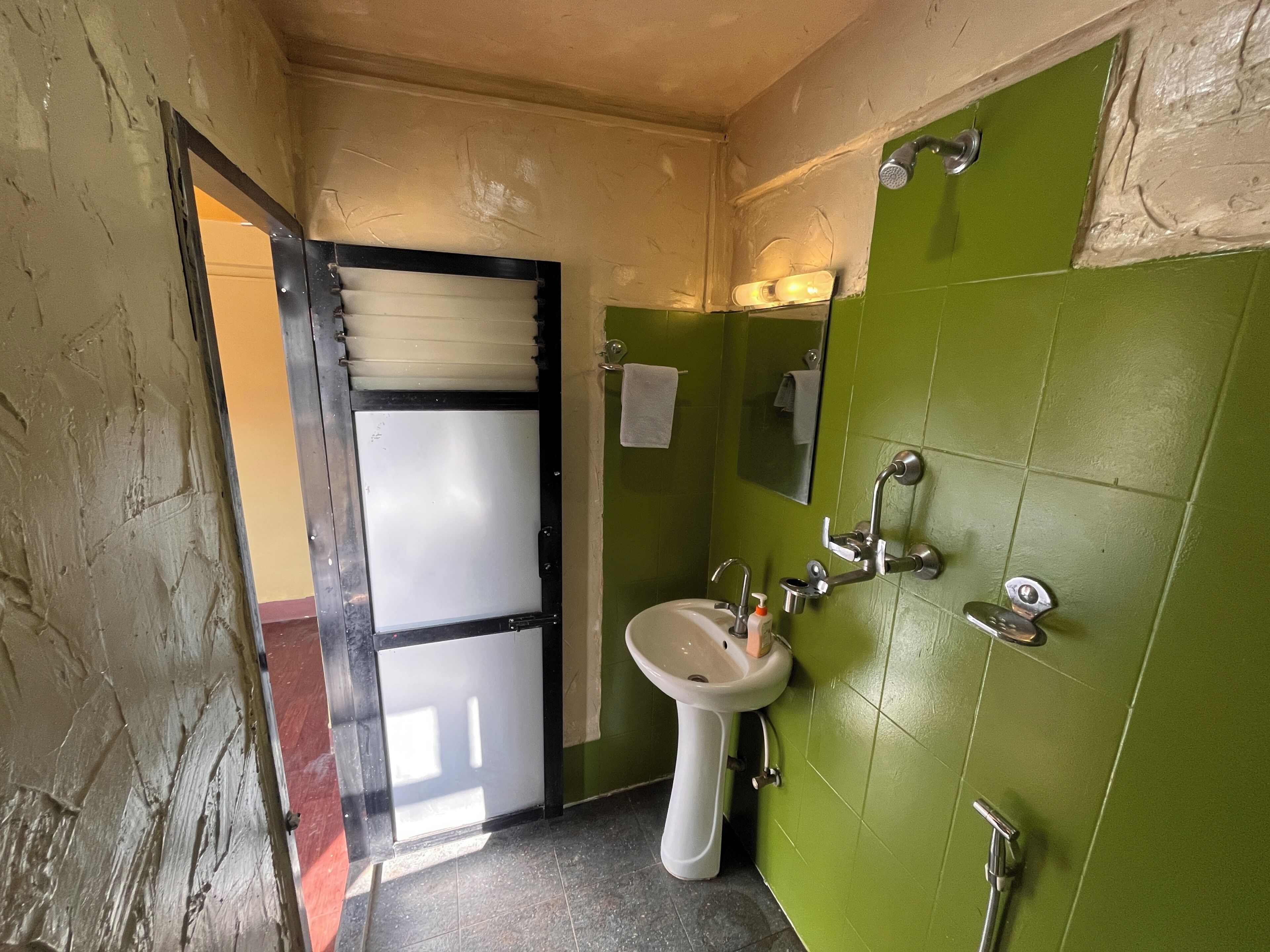 A bathroom with a green tiled wall, a white sink, and a shower with a handheld showerhead.