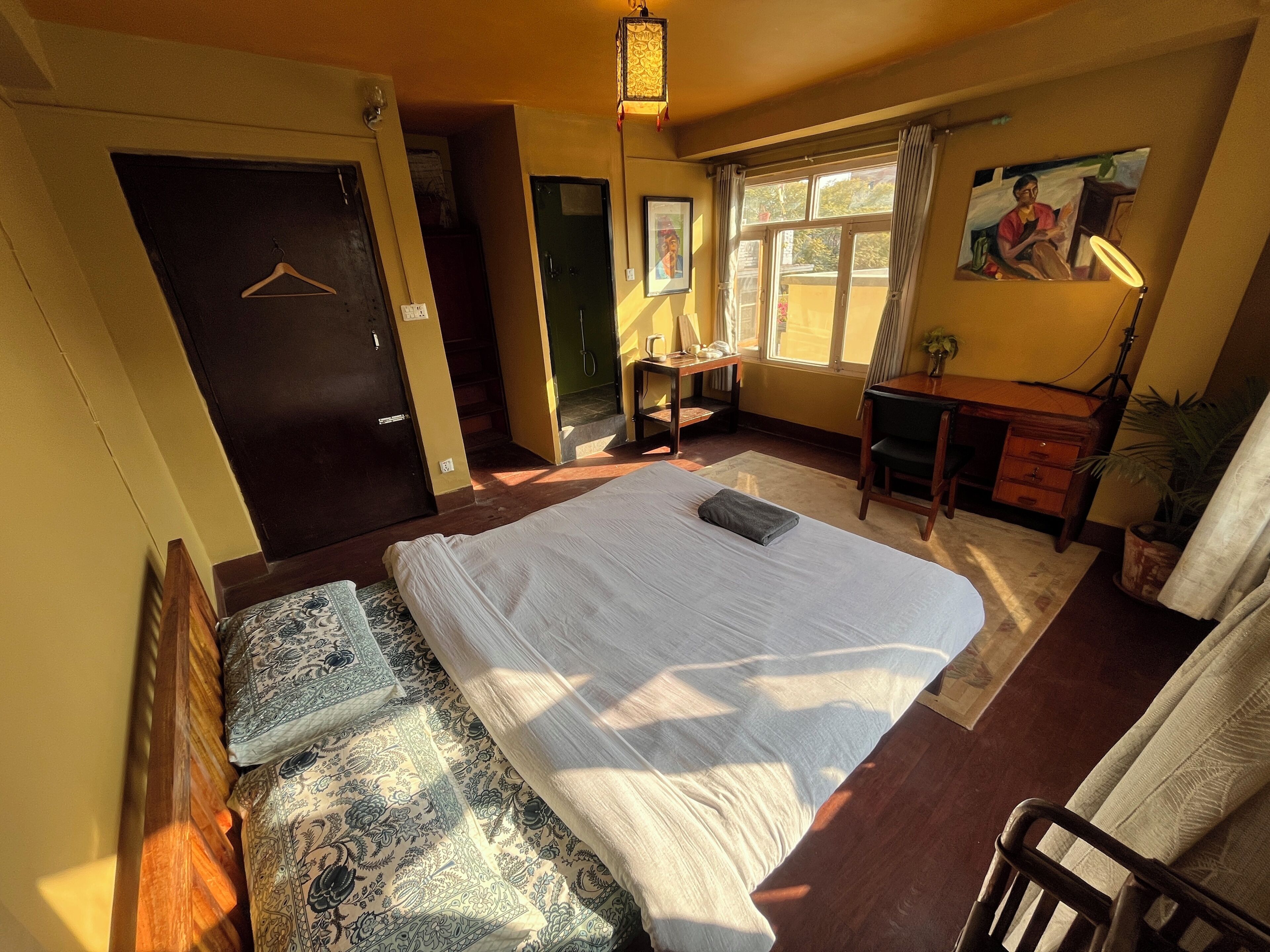 A bedroom with a large bed, a desk, a chair, a door, and a window with curtains.