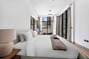 A hotel room with a large bed, a bedside table, a lamp, a chair, and a view of the city through large windows. - StayShort - 1 Bed in Business Bay that Sleeps 2 with Balcony! (Business Bay)