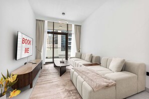 A modern living room with a sofa, a coffee table, a TV mounted on the wall, and a view of the city through large windows. - StayShort - 1 Bed in Business Bay that Sleeps 2 with Balcony! (Business Bay)