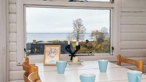 Ein Essbereich mit einem Tisch für vier Personen, einem Fenster mit Meerblick und einem gerahmten Bild auf dem Tisch.