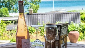 Eine Weinflasche, zwei Weingläser und ein Buch mit dem Titel 'The Empty Chair' auf einem Tisch mit Meerblick.