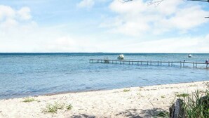 Ein Strand mit klarem Wasser, sandigem Ufer und einem Steg, der ins Meer führt.