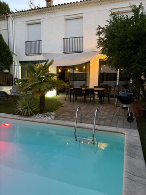 Ein Pool mit Stufen, eine Terrasse mit Gartenmöbeln und ein weißes Gebäude mit Fensterläden.
