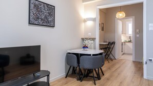 Una sala de estar moderna con un televisor de pantalla plana, una mesa de comedor con sillas, un jarrón con flores y un cuadro en la pared.