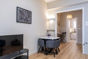 A modern living room with a flat-screen TV, a dining table with chairs, a vase with flowers, and a painting on the wall. - Charming 2BR Downtown Metro (Athina)
