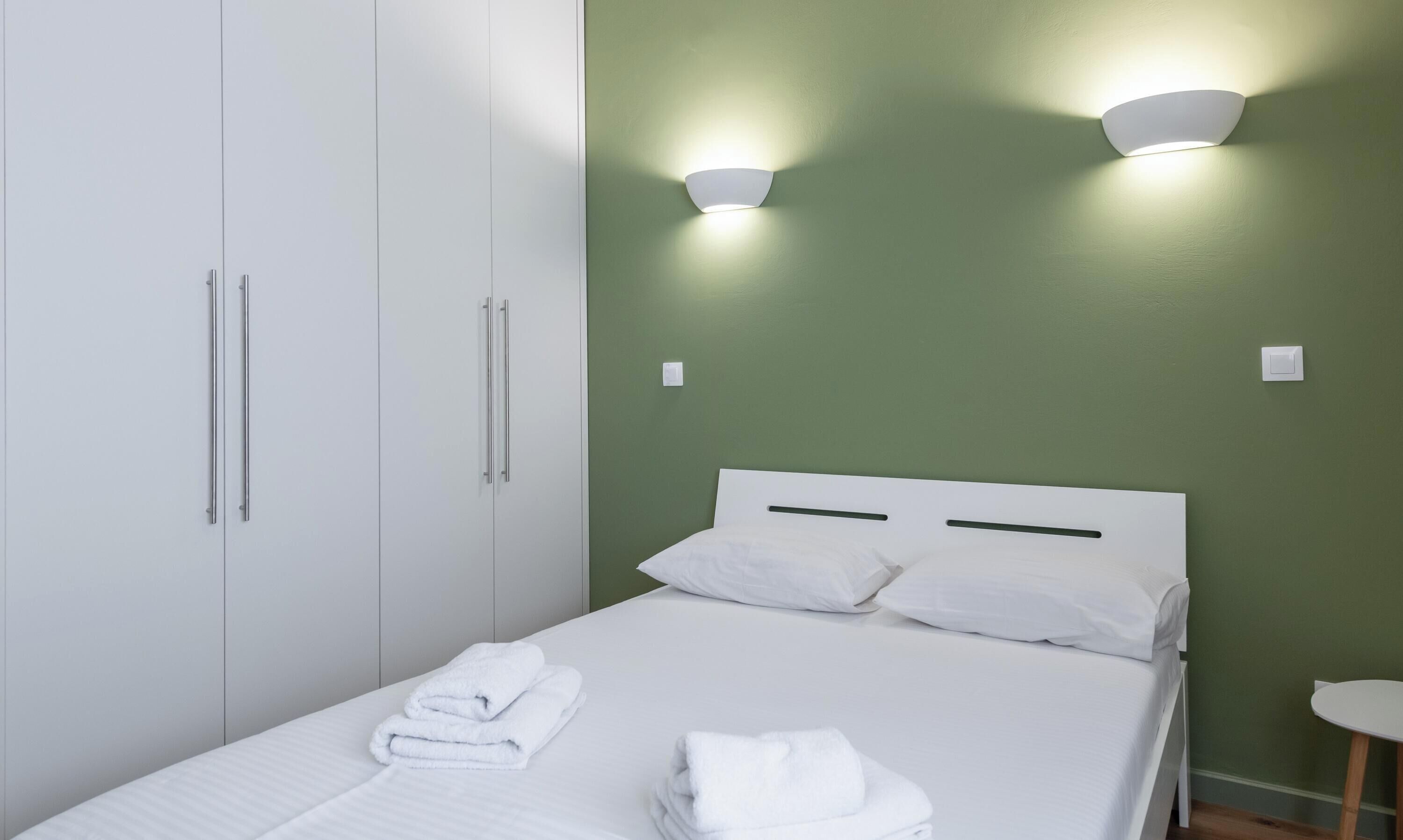 Una habitación de hotel con cama, cortinas blancas, un armario y dos luces fijadas a la pared.