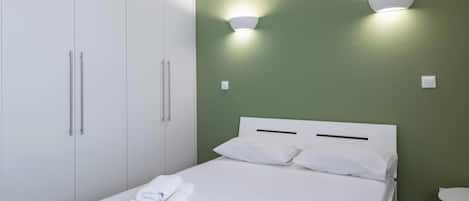 Una habitación de hotel con cama, cortinas blancas, un armario y dos luces fijadas a la pared.