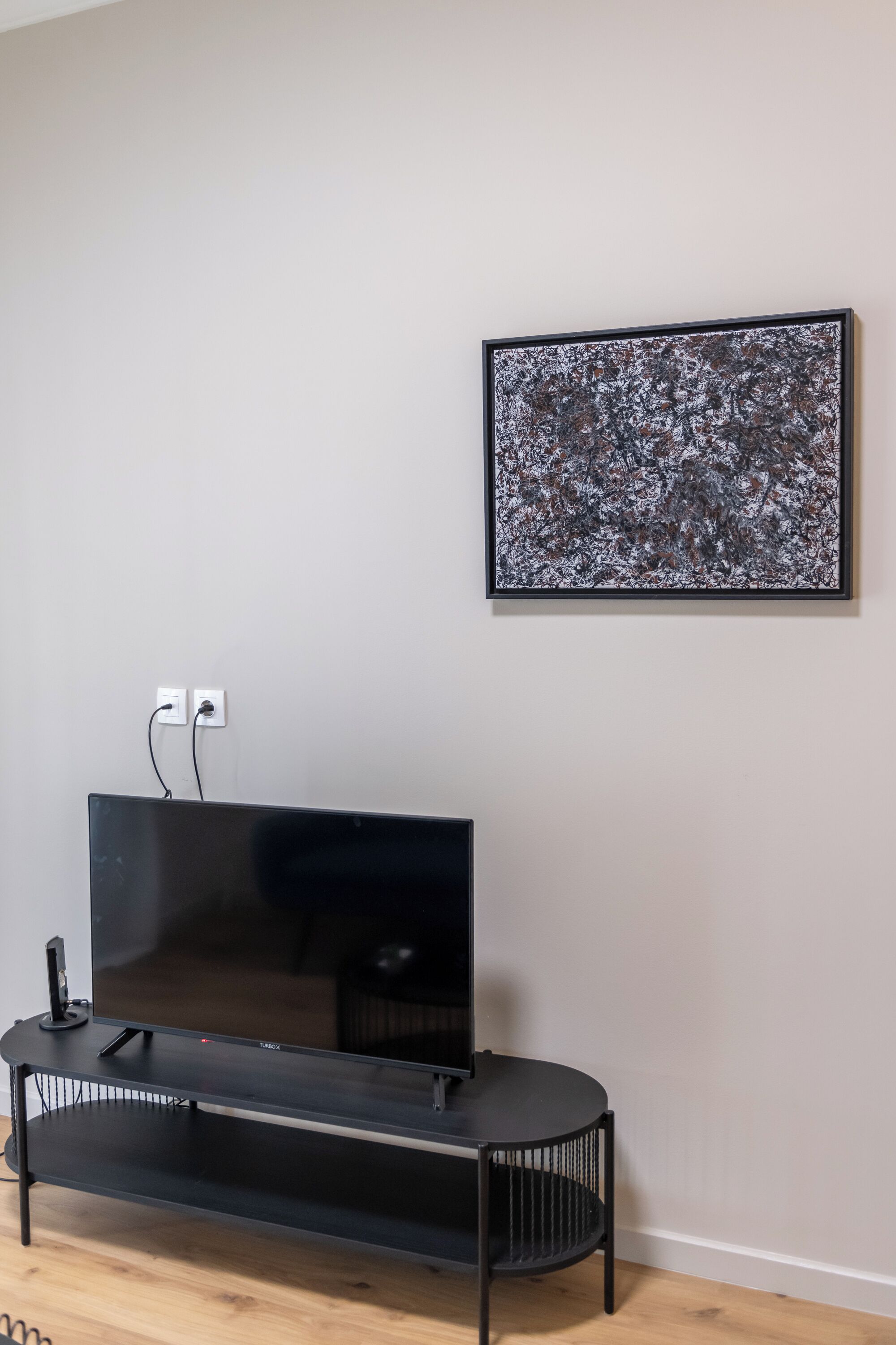 Ein Flachbildfernseher auf einem schwarzen Ständer an einer Wand, mit Steckdose und Kabel zu sehen.