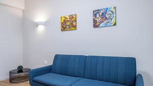 Una habitación con un sofá azul, dos cuadros abstractos en la pared, una pequeña mesa negra y una lámpara.