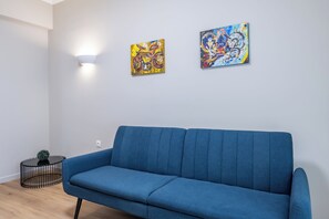 A room with a blue sofa, two abstract paintings on the wall, a small black table, and a light fixture. - Charming 2BR Downtown Metro (Athina)