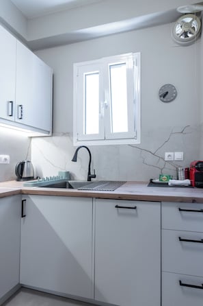 A modern kitchen with white cabinets, a stainless steel sink, a kettle, and a red appliance. - Charming 2BR Downtown Metro (Athina)