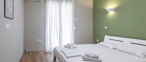 A hotel room with a bed, white curtains, an air conditioning unit, and a wall-mounted light fixture.