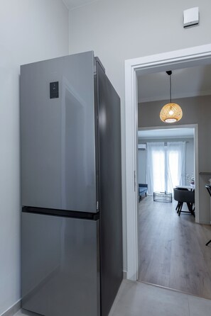 A modern kitchen with a stainless steel refrigerator, a dining area with a table and chairs, and a hanging light fixture. - Charming 2BR Downtown Metro (Athina)