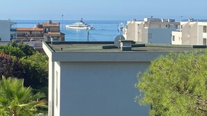 Rannikkoalue, jossa on asuintaloja, lahdella ankkuroituna oleva jahti, tasakattoisia rakennuksia ja vehreää kasvillisuutta.