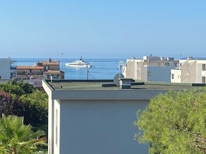 Ein Küstenwohngebiet mit einer Yacht im Wasser, Gebäuden mit flachen Dächern und Grünflächen.