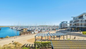 Eine Marina mit zahlreichen angestuften Booten, ein Strandabschnitt mit überdachter Sitzgelegenheit und ein modernes Gebäude mit Balkonen.