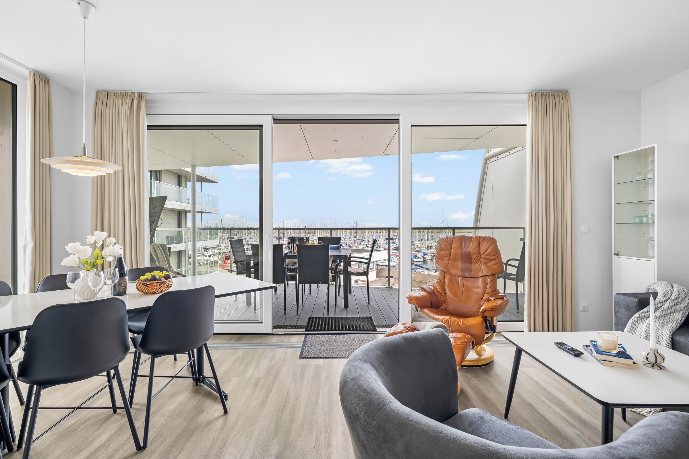 Ein modernes Wohnzimmer mit Essbereich, einem großen Fenster mit Blick auf die Marina und einem Ledersessel.