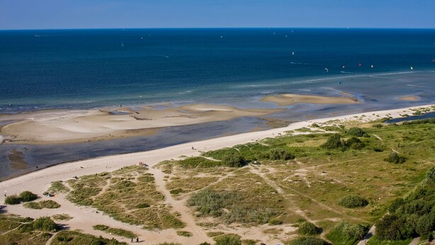 Eine Küstenlandschaft mit Sandstrand, grasbewachsenen Dünen und blauem Himmel.