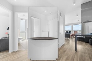 Ein modernes Interieur mit einer zentralen, weißen Schrankeinrichtung, einem Essbereich mit Ausblick und einer Küche mit großem Fenster.