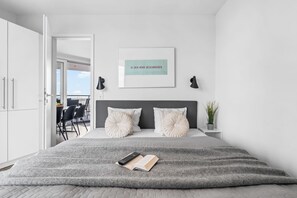 Ein modernes Schlafzimmer mit einem großen Bett, einem gerahmten Zitat an der Wand und Blick ins Freie.