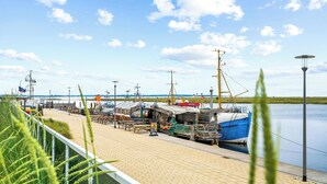 Eine Hafenpromenade mit Booten, einem Steg und blauem Himmel.
