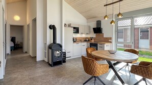 A modern kitchen with a wood-burning stove, white cabinets, and a dining area with a round table and chairs. - Newly Built Vacation Home "Wiesengeflüster W1" | With Garden, Indoor Sauna, and Fireplace (Röbel)