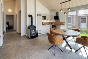 Eine moderne Küche mit Kaminofen, weißen Schränken und einem Essbereich mit rundem Tisch und Stühlen.