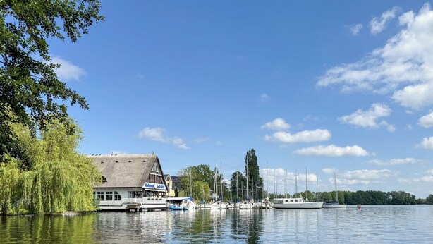 Een gebouw aan de rivier met rieten dak, aangemeerde boten en een rustig waterlichaam met waterlelies.