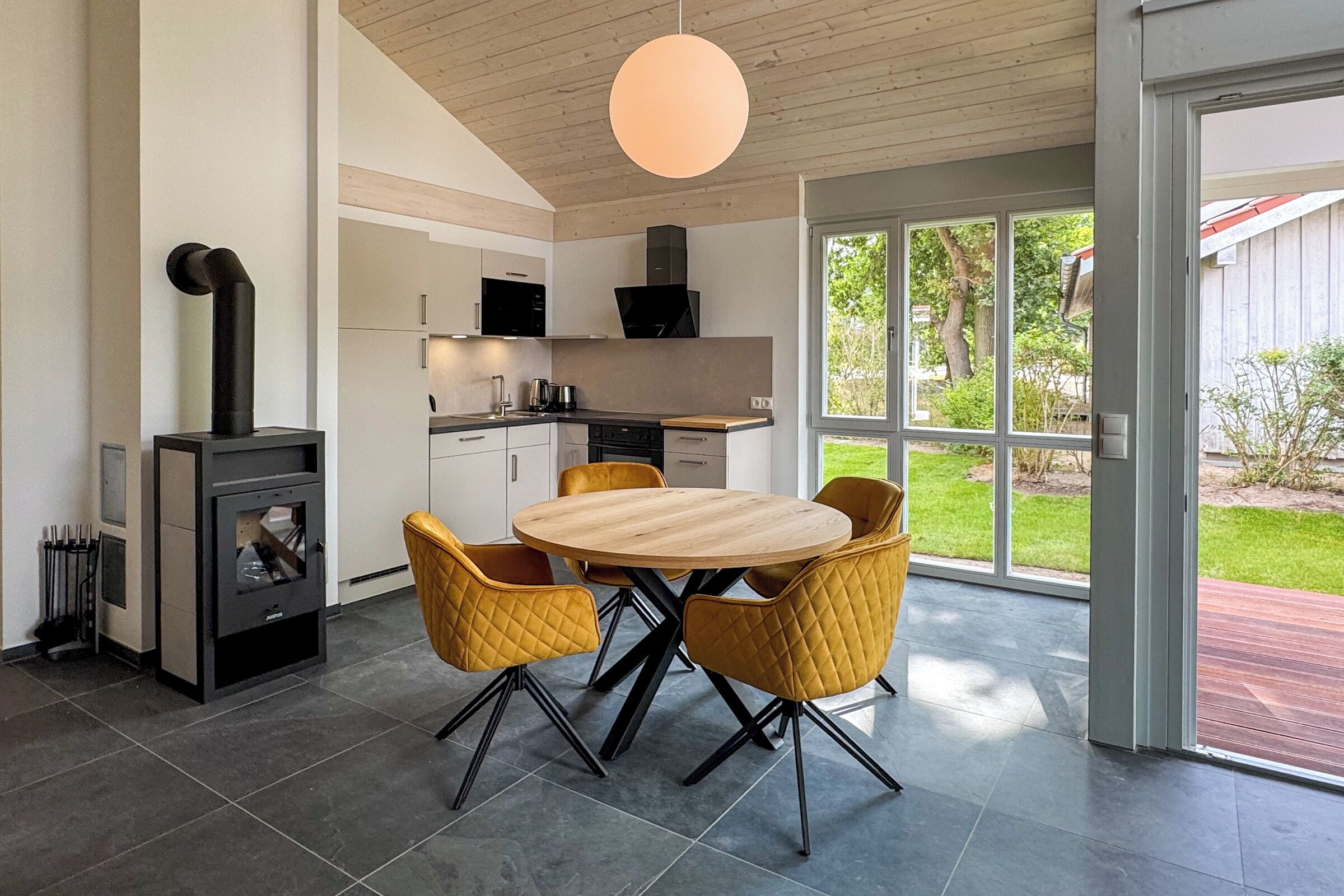 Una cocina moderna con zona de comedor, ventanas amplias y estufa de leña.