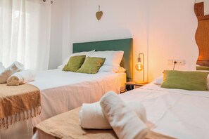 Habitación de hotel con dos camas, una mesita de noche con lámpara y un adorno de corazón en la pared.