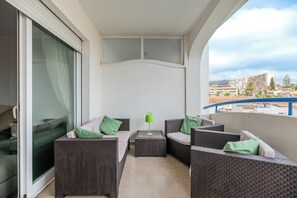 Un balcón con mobiliario de mimbre, una lámpara verde y vistas a edificios.