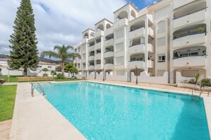 Una piscina con agua cristalina azul, rodeada por un edificio blanco con balcones y una palmera.