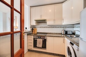 Una cocina moderna con armarios blancos, horno empotrado, lavadora y encimera de granito.