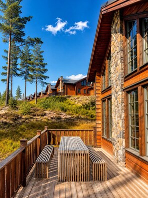 A wooden deck with a table and benches, overlooking a mountainous landscape with pine trees.