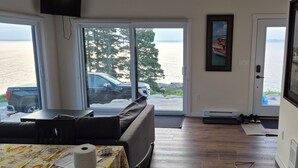 A room with a sofa, a table with a floral tablecloth, a door leading outside, and a framed picture on the wall. - Brand-new Oceanfront cottage 8 overlooking Peggys Cove. (Hubbards)