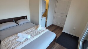 A neatly made bed with a patterned bedspread and pillows, a bedside table with a book, and a door leading to a bathroom. - Brand-new Oceanfront cottage 8 overlooking Peggys Cove. (Hubbards)
