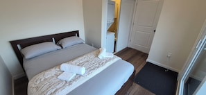 Una cama bien hecha con colcha y almohadas estampadas con motivos florales, una mesita de noche con lámpara y una puerta que da a un baño.