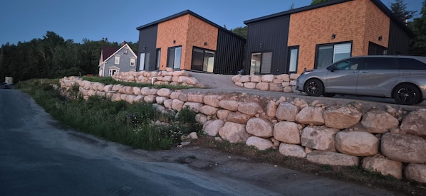 Una casa moderna de dos pisos con un muro de contención de piedra y un coche aparcado.