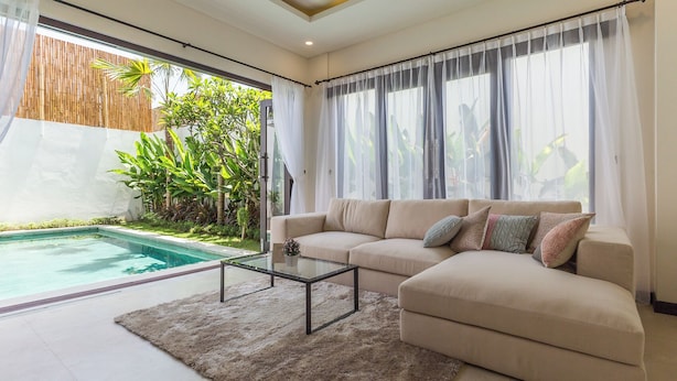 A living room with a beige sofa, a glass coffee table, and a view of a swimming pool. - Villa Sereine Seminyak (Seminyak)