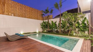 A swimming pool with a wooden deck and tropical plants. - Villa Sereine Seminyak (Seminyak)