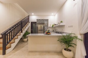 A modern kitchen with a central island, a built-in refrigerator, and a staircase leading to another level. - Villa Sereine Seminyak (Seminyak)