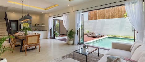 A modern living room with a pool, dining area, and kitchen.