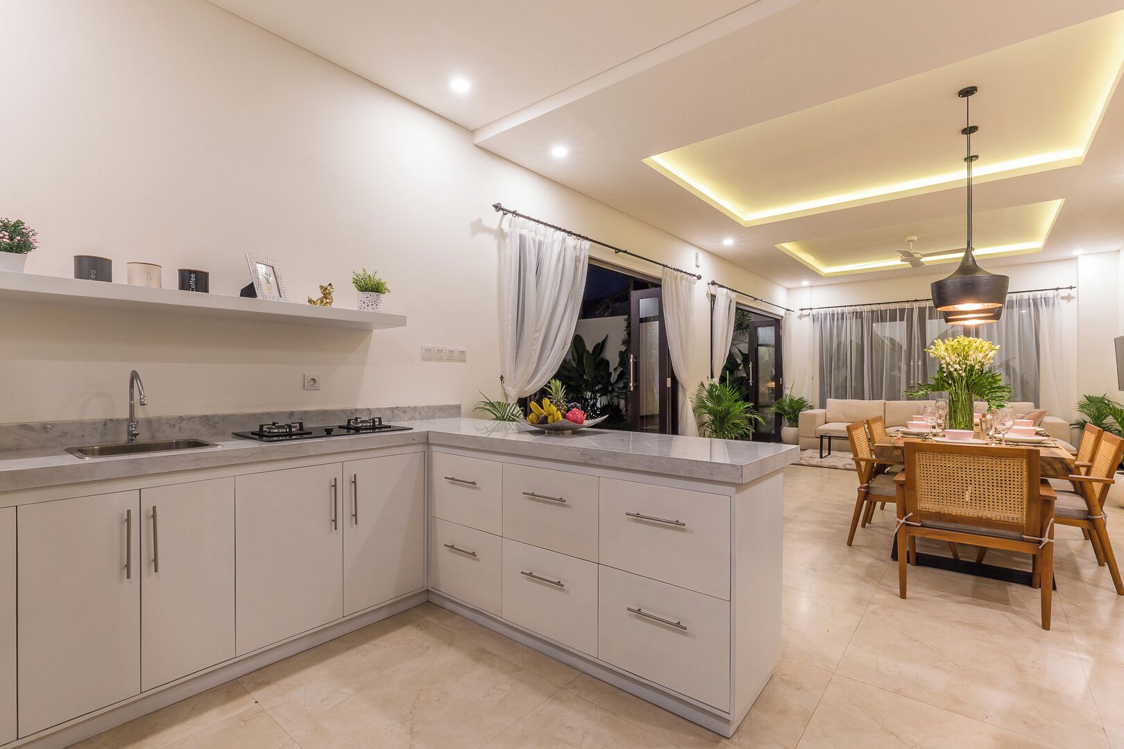A modern kitchen with a built-in island, a dining area with a table and chairs, and a living room with a sofa and a ceiling light fixture.