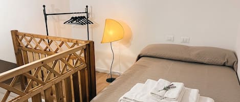 Un dormitorio con cama, una silla de madera, una lámpara y un tendedero en la pared.