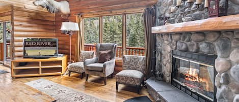 A log cabin interior with a stone fireplace, a mounted deer head, and a sign reading 'Red River.'