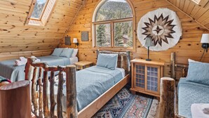 Een slaapkamer in een blokhut met een hoogslaper, een houten kast en een groot raam met uitzicht op de bergen.