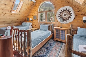A log cabin bedroom with a loft bed, a wooden cabinet, and a large window with a mountain view. - Riverfront Log Cabin "River Chant Lodge" Hot Tub, on the River, Fire Pit; Under New Management (Red River)