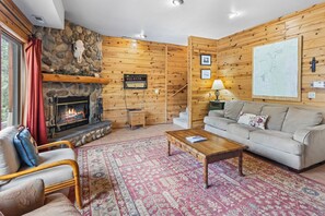 Ein gemütliches Wohnzimmer mit Kamin aus Stein, Holzwänden, einer Couch, einem Couchtisch und einem Teppich.