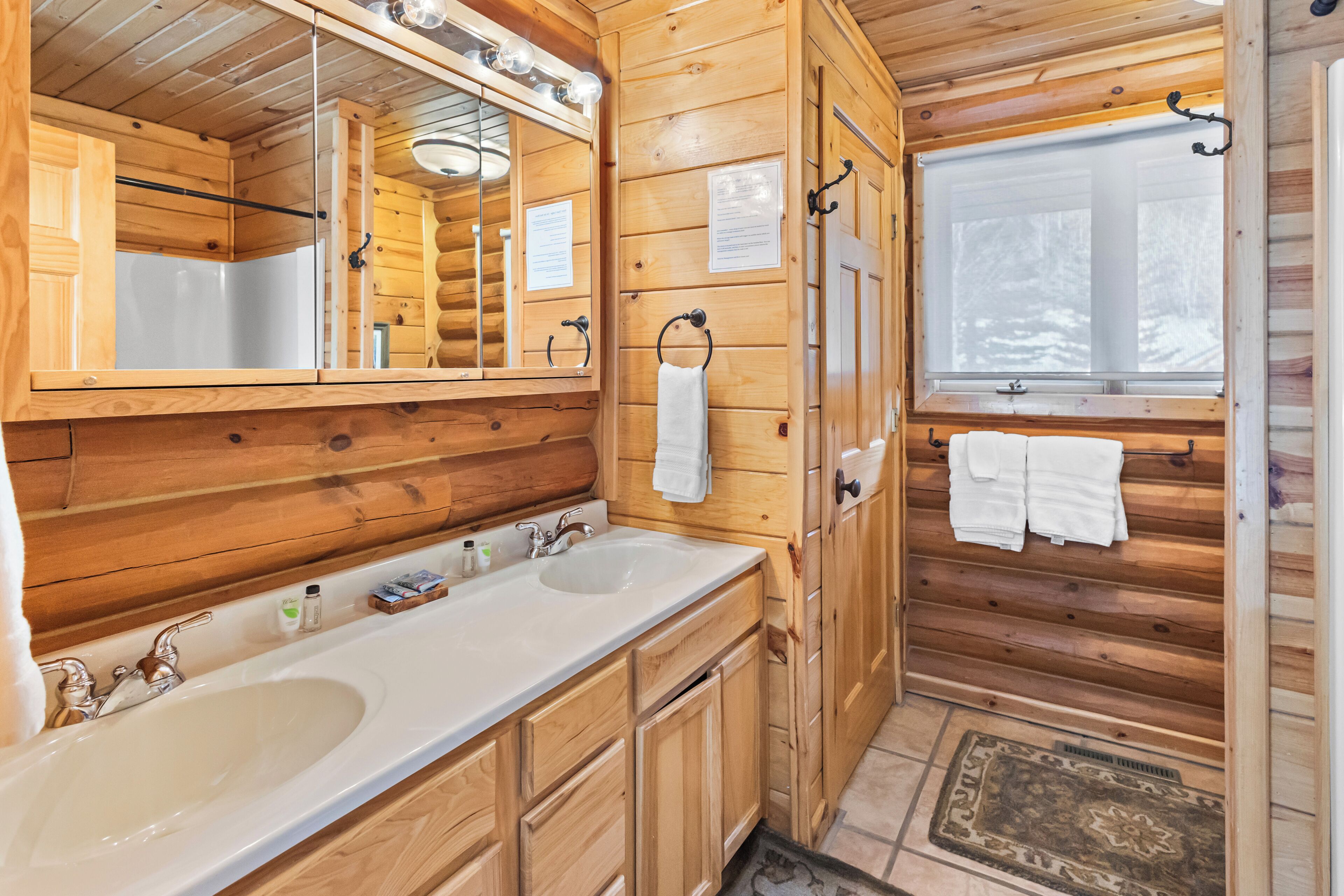 A wooden cabin bathroom with two sinks, a mirror, and a window.
